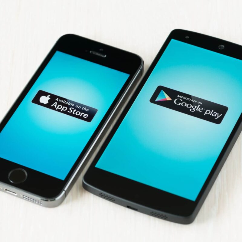 App Store und Google Play Store Logos abgebildet auf zwei Smartphones