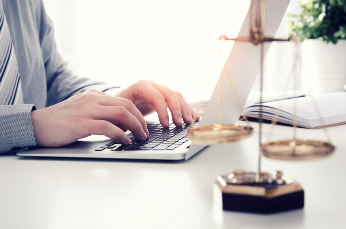 Männerhände tippen auf Laptop, im Vordergrund steht eine goldene Waage