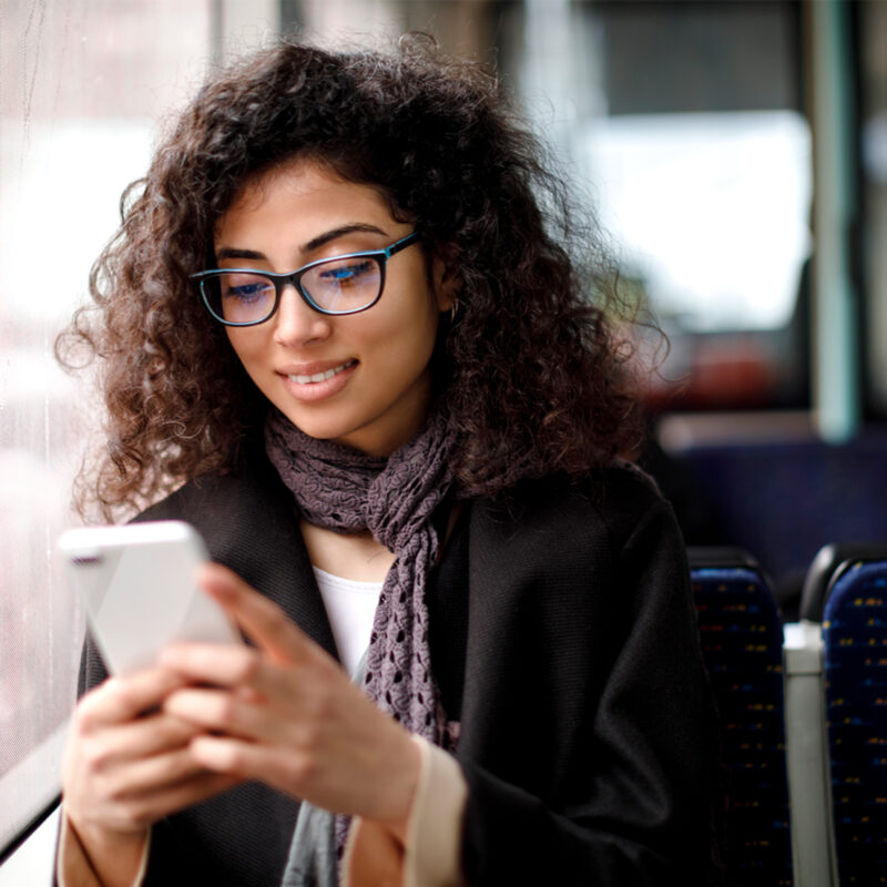 Frau im öffentlichen Verkehrsmittel schaut auf ihr Handy