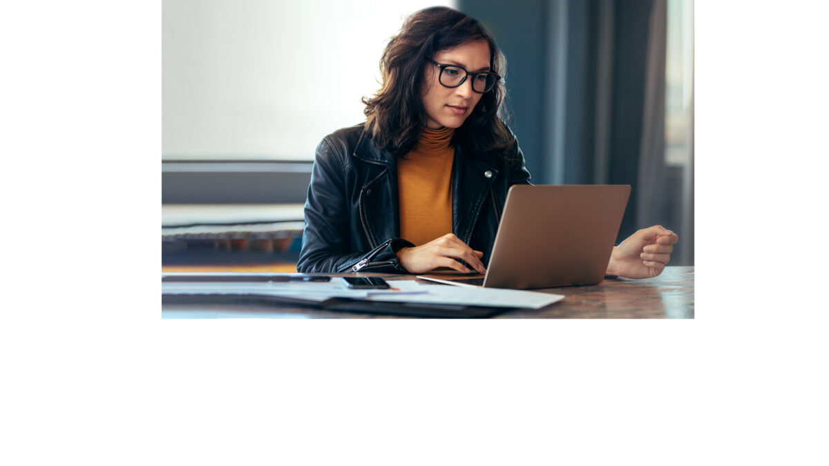 Frau sitzt in Blazer und Pulli vor Laptop