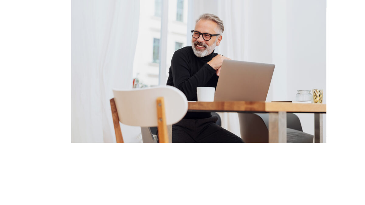Grauhaariger Mann mit Bart und Brille sitzt vor Laptop