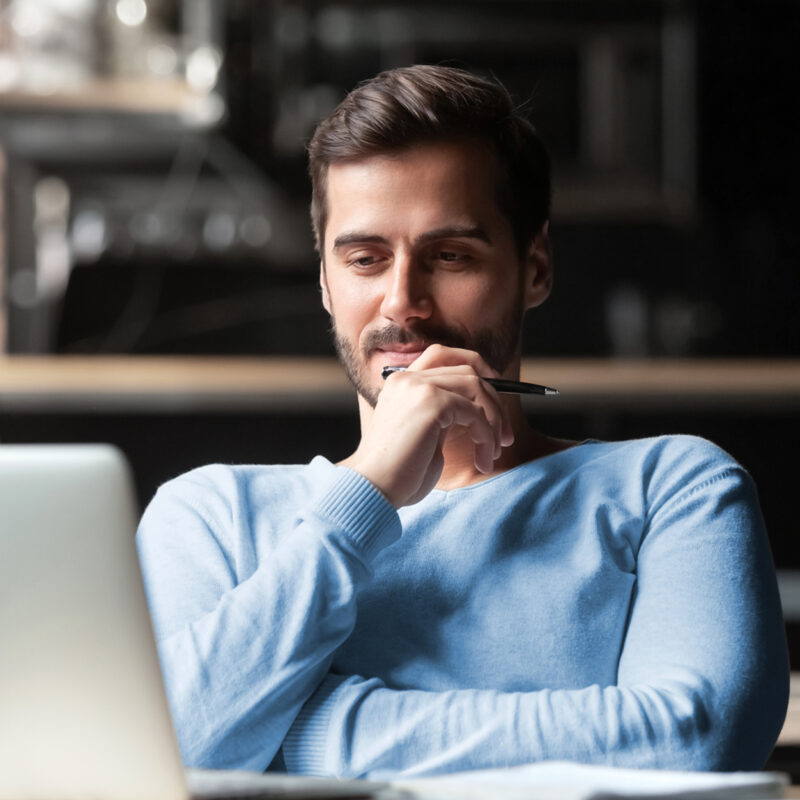 Man with pen in hand sits in front of laptop