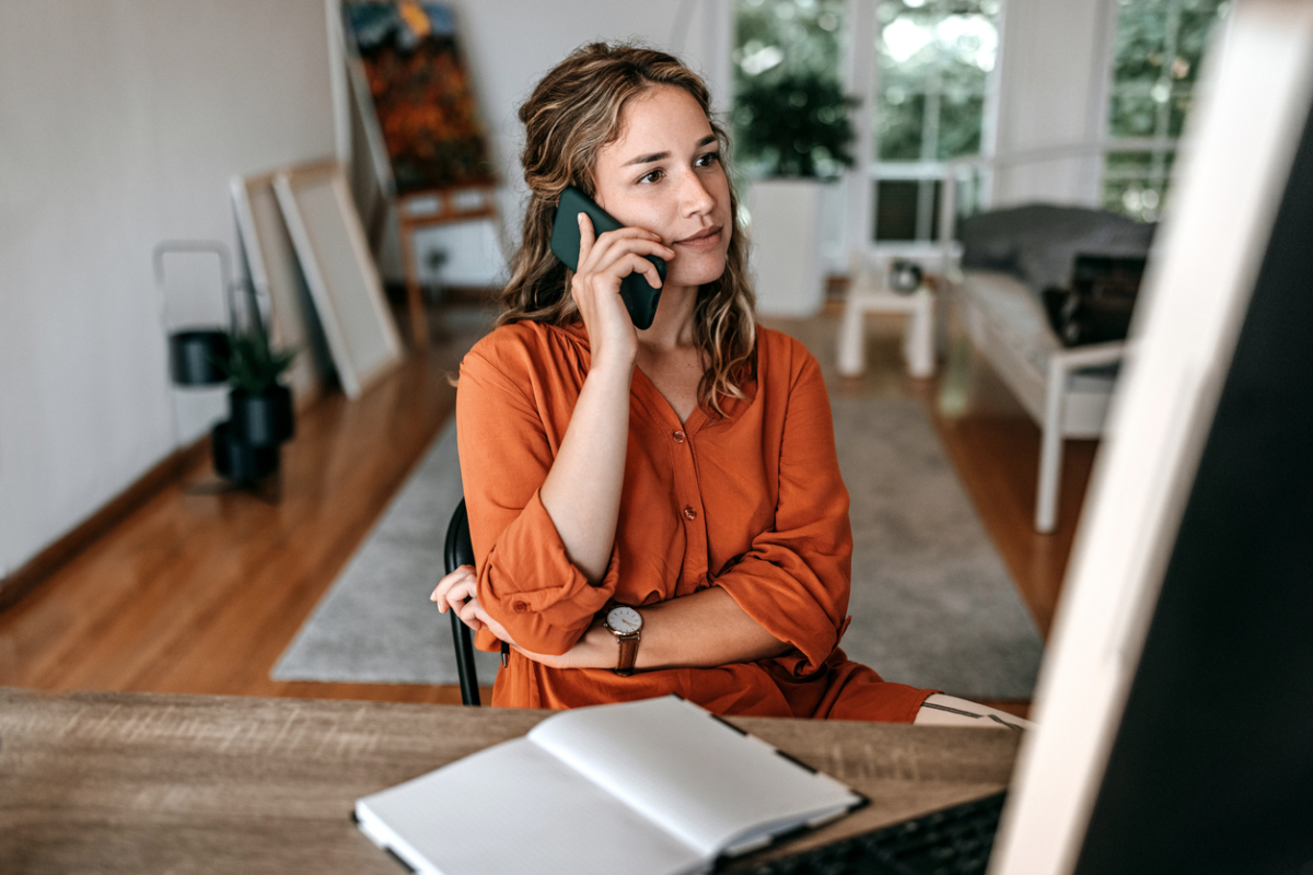 Woman in orange shirt sitting at desk and talking on phone