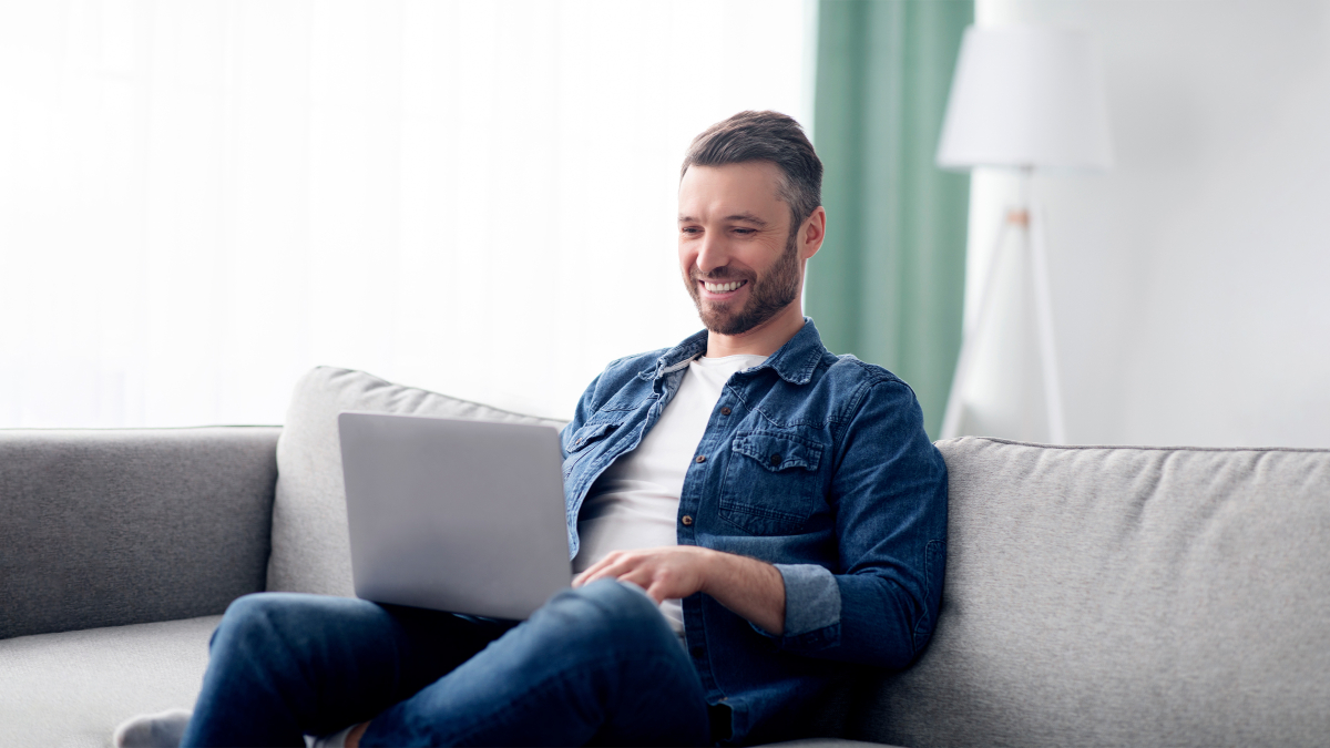 Mann sitzt mit Laptop auf einer Couch