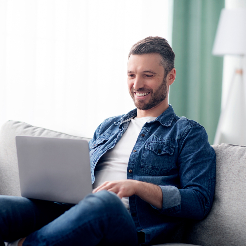 Mann sitzt mit Laptop auf einer Couch