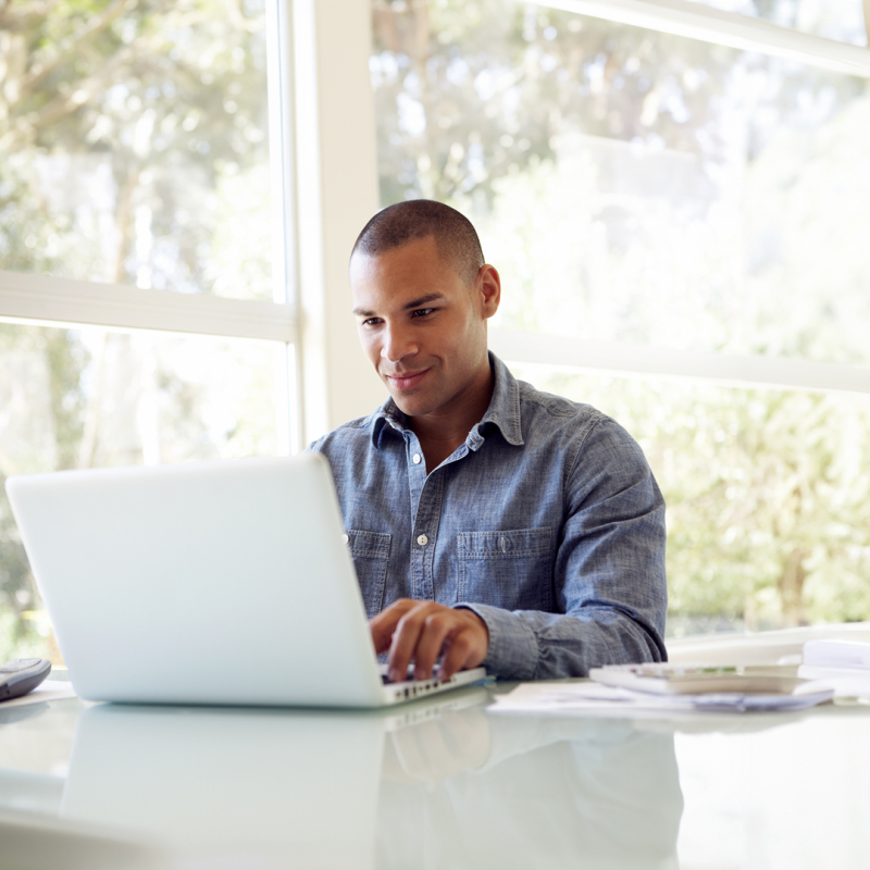 Mann tippt am Laptop vor Fenster