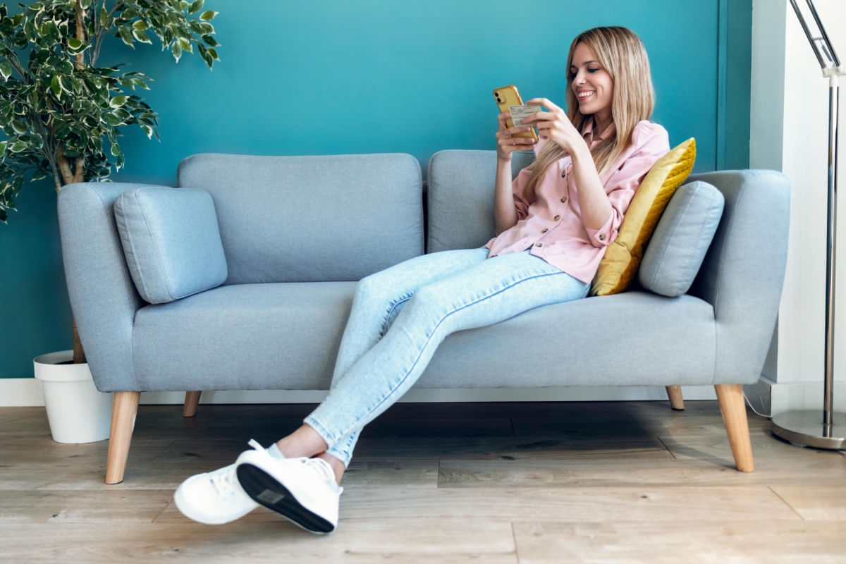Junge Frau beim Online-Shopping mit Personalausweis und Smartphone, während sie zu Hause auf dem Sofa sitzt