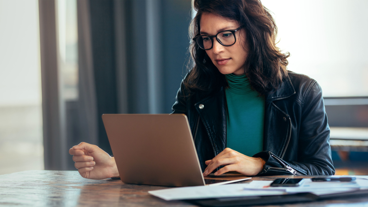 Frau mit dunklen Haaren und Brille am Schreibtisch und Laptop